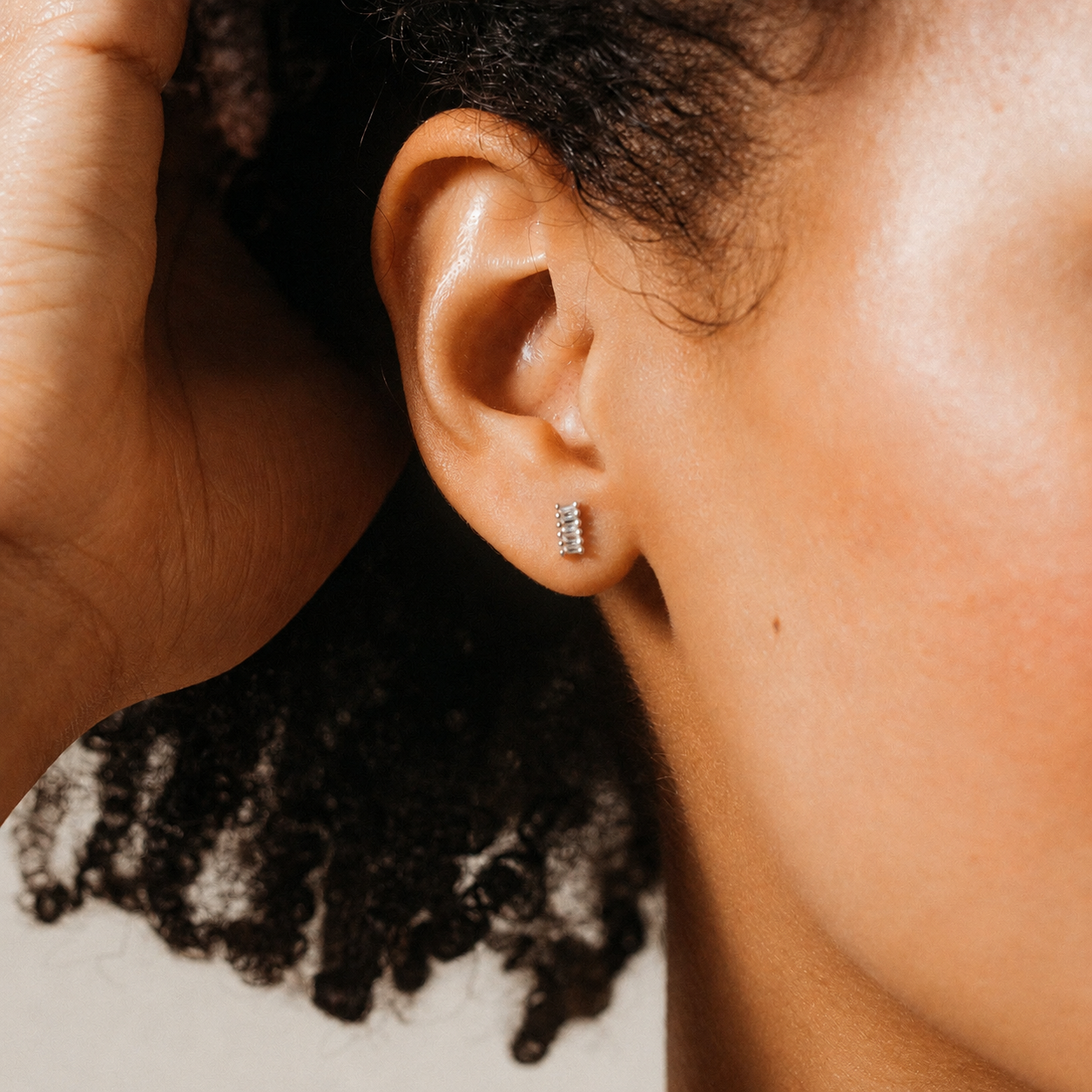 Close-up of an ear with a small hoop earring, hand holding hair.