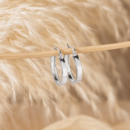 Silver hoop earrings on a wooden stick against a soft, blurred background