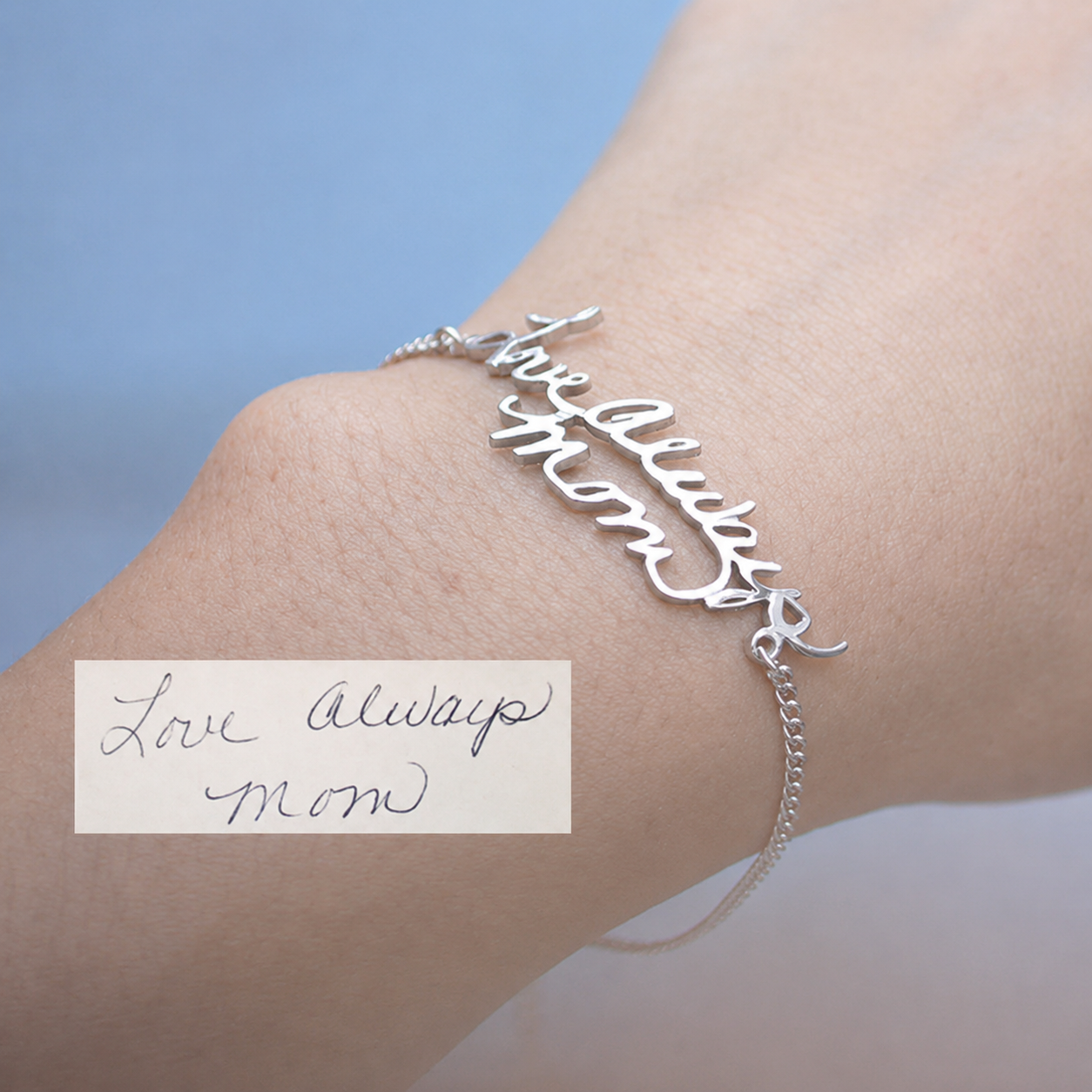 Silver bracelet with 'love always mom' on wrist against a blue background