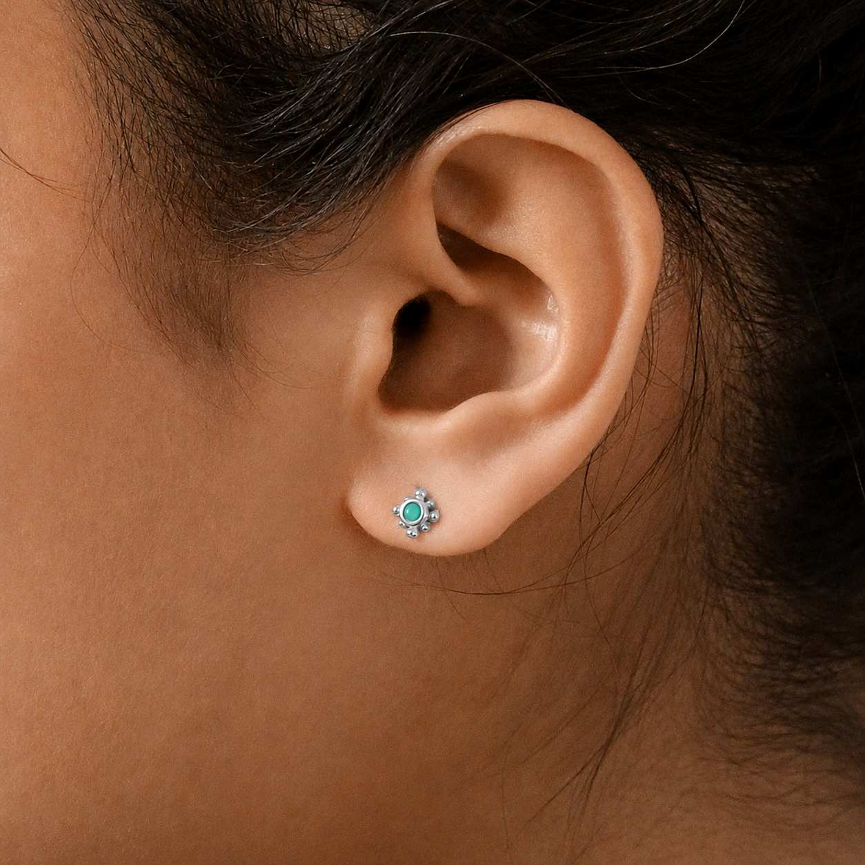 Close-up of an ear wearing a small earring with a green gemstone.