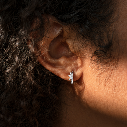 A close-up of a person's ear wearing a small silver crescent moon stud earring, with warm sunlight highlighting the skin and dark curly hair.