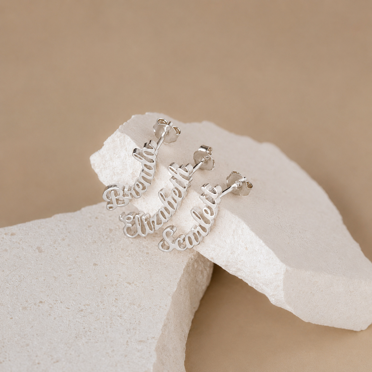 Silver earrings with engraved text on a beige background