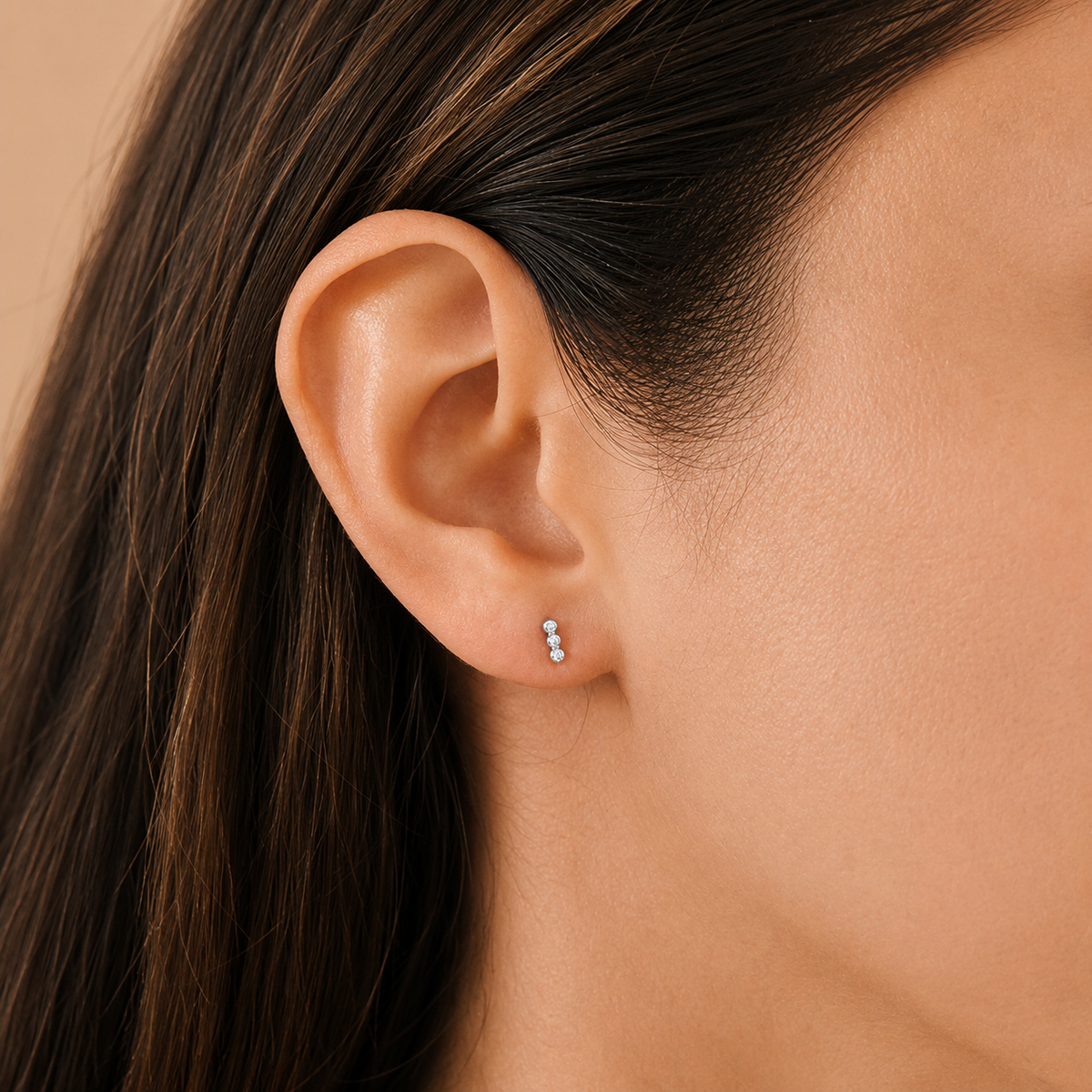 Close-up of an ear wearing a small earring with dark hair and skin background