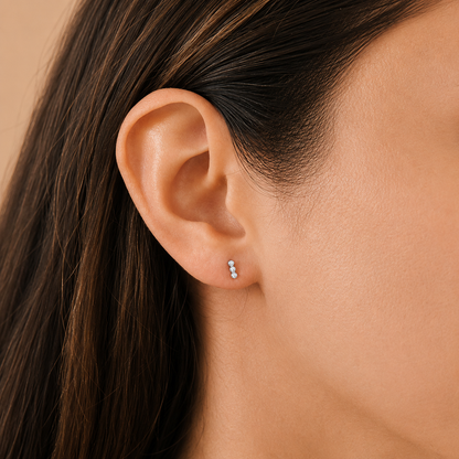 Close-up of an ear wearing a small earring with dark hair and skin background
