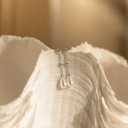 Silver earrings with teardrop-shaped pearls on a textured beige surface