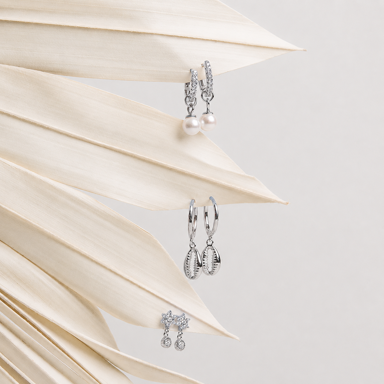 Silver hoop earrings with pearl and crystal details on a light background with leaves.