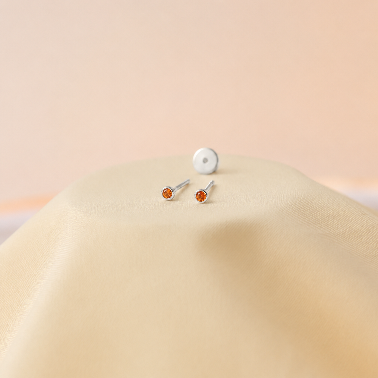 Two silver stud earrings with orange gemstones on a beige surface.