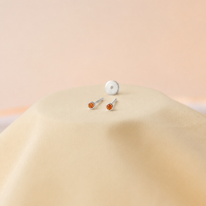 Two silver stud earrings with orange gemstones on a beige surface.