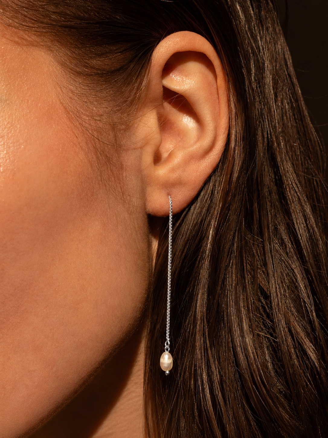 Close-up of an ear wearing a pearl drop earring with a blurred background