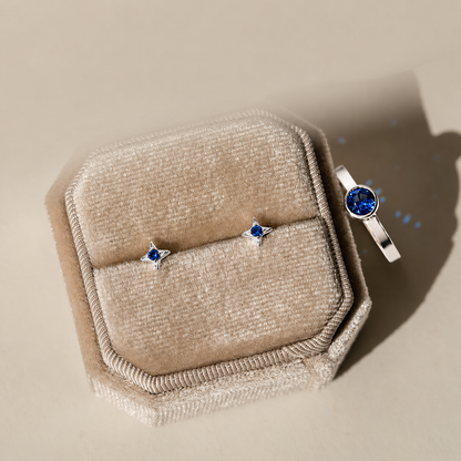 Silver ring and earrings with blue gemstones on a beige jewelry box.