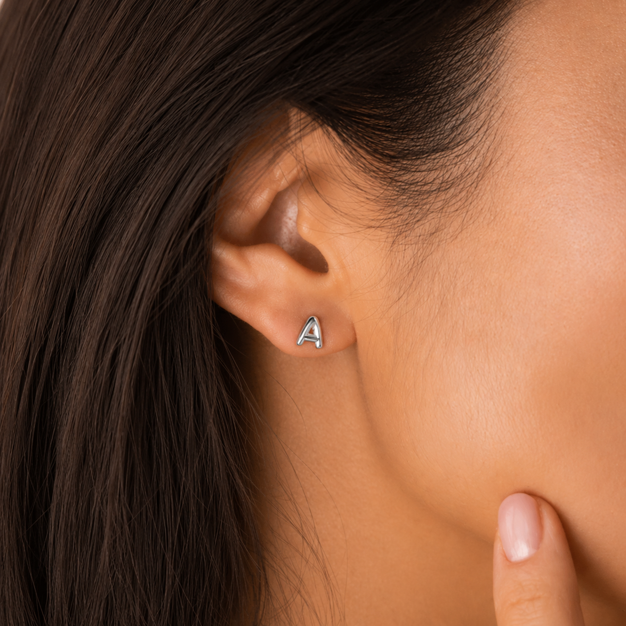 Close-up of an ear wearing a silver 'A' earring with dark hair and skin in the background.