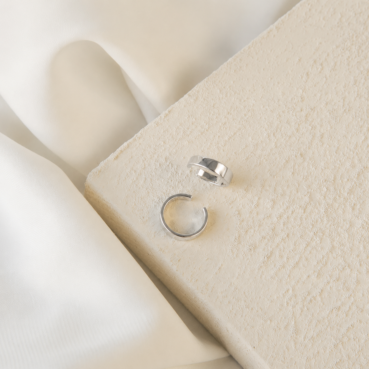 Two silver rings on a textured beige surface