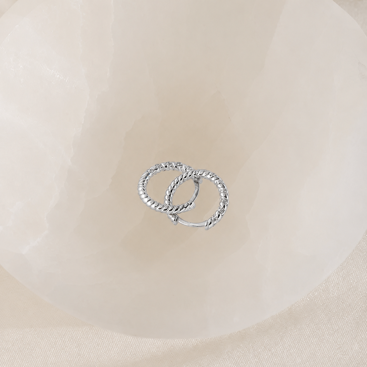 Two silver hoop earrings on a beige fabric background