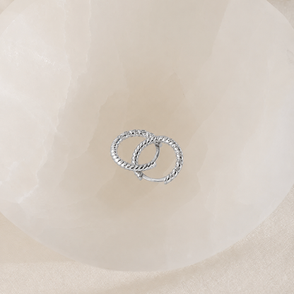Two silver hoop earrings on a beige fabric background