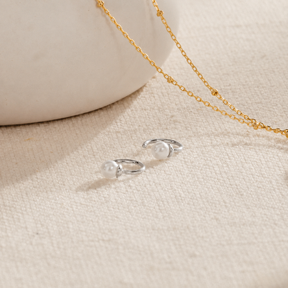 Silver earrings with a gold chain on a beige fabric background