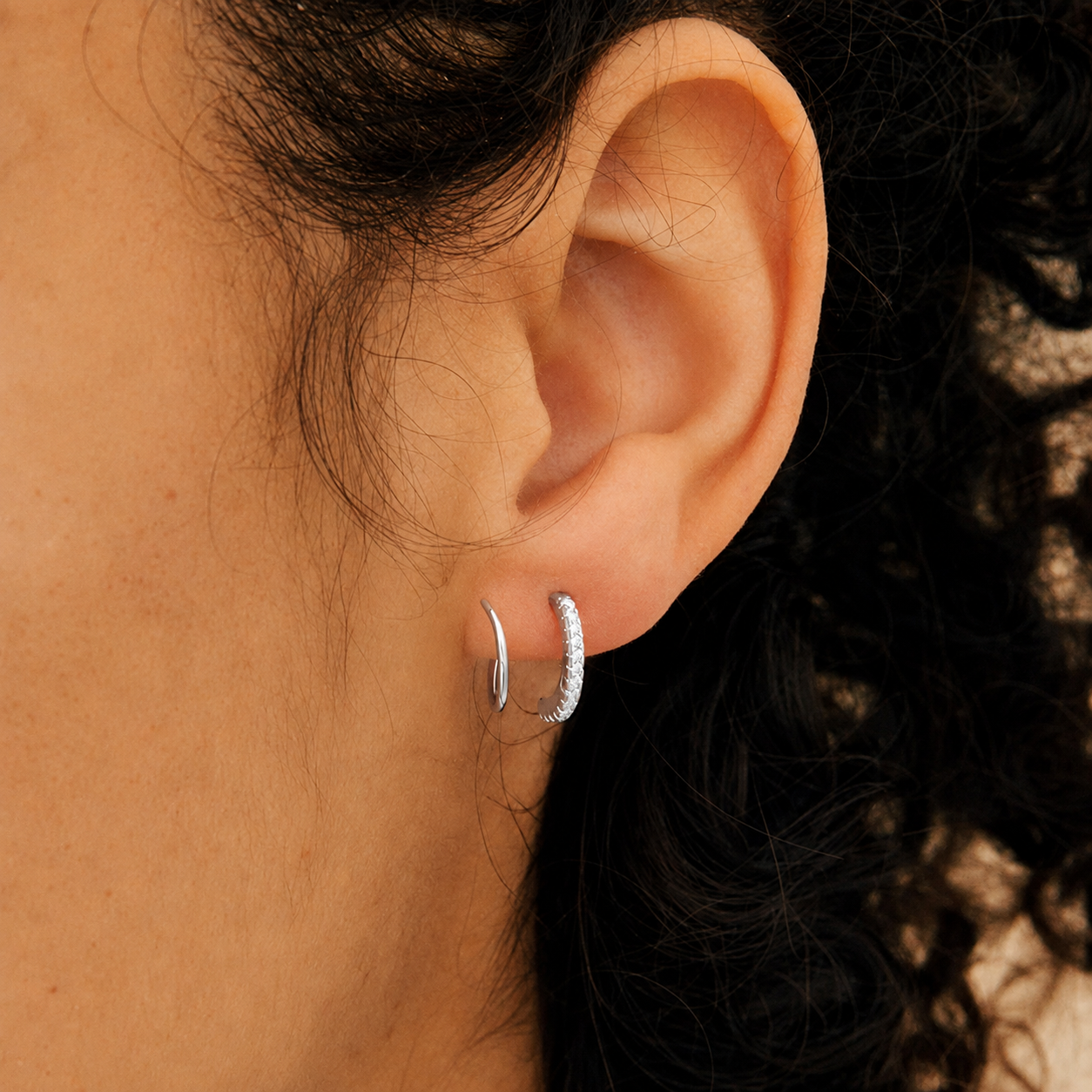 Close-up of an ear wearing silver hoop earrings with a blurred background