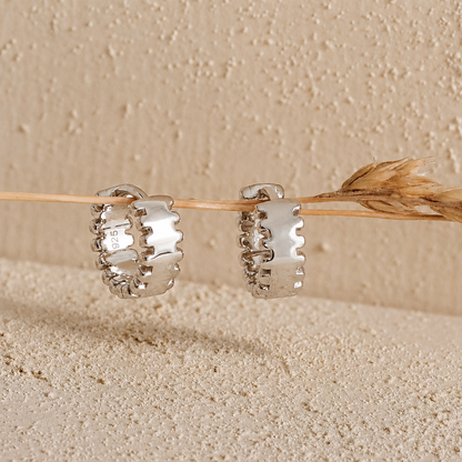 Silver hoop earrings on a wooden stick against a beige background
