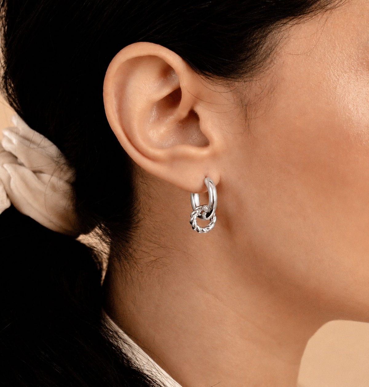 Close-up of an ear wearing a silver hoop earring with a blurred background