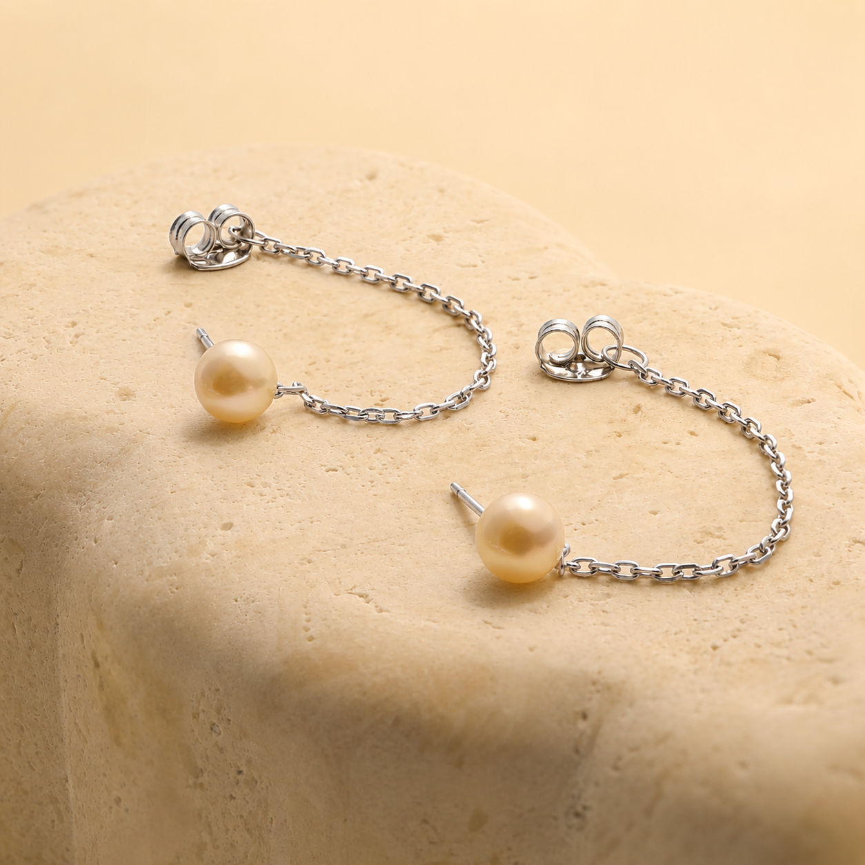 Pearl earrings with silver chains on a beige surface