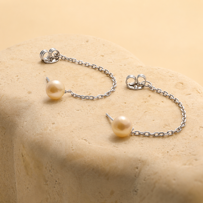 Pearl earrings with silver chains on a beige surface
