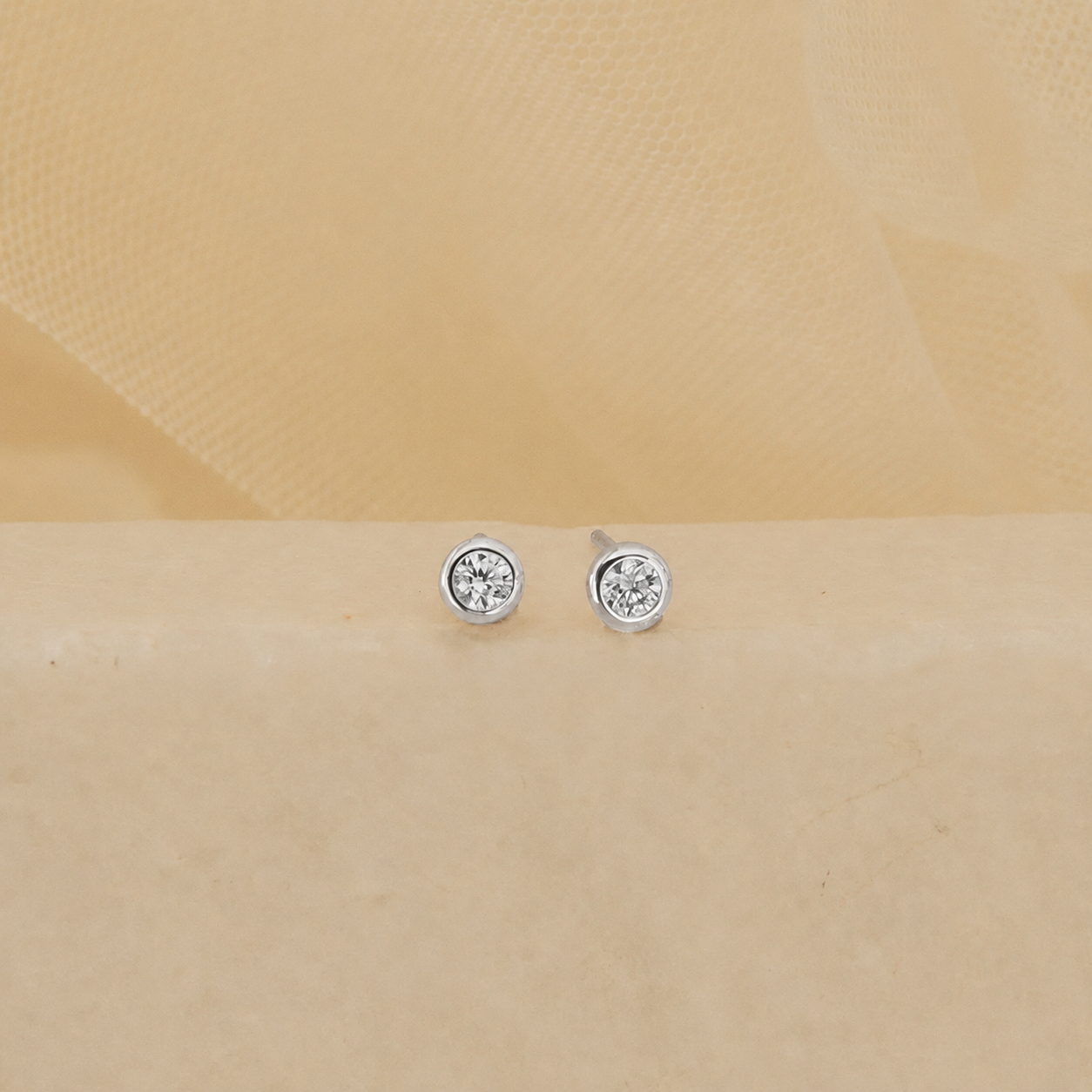 Pair of silver stud earrings with clear gemstones on a beige background