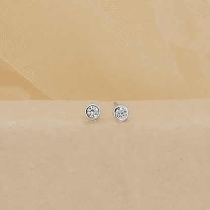 Pair of silver stud earrings with clear gemstones on a beige background