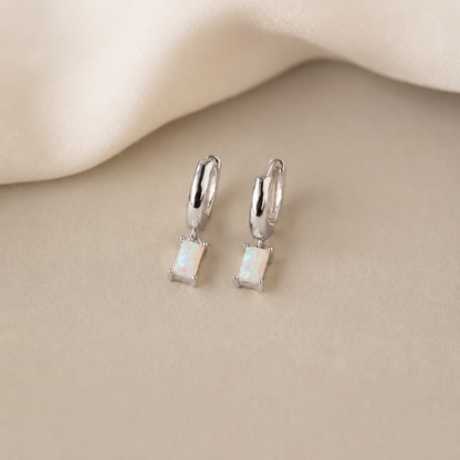 Pair of silver earrings with gemstones on a beige fabric background