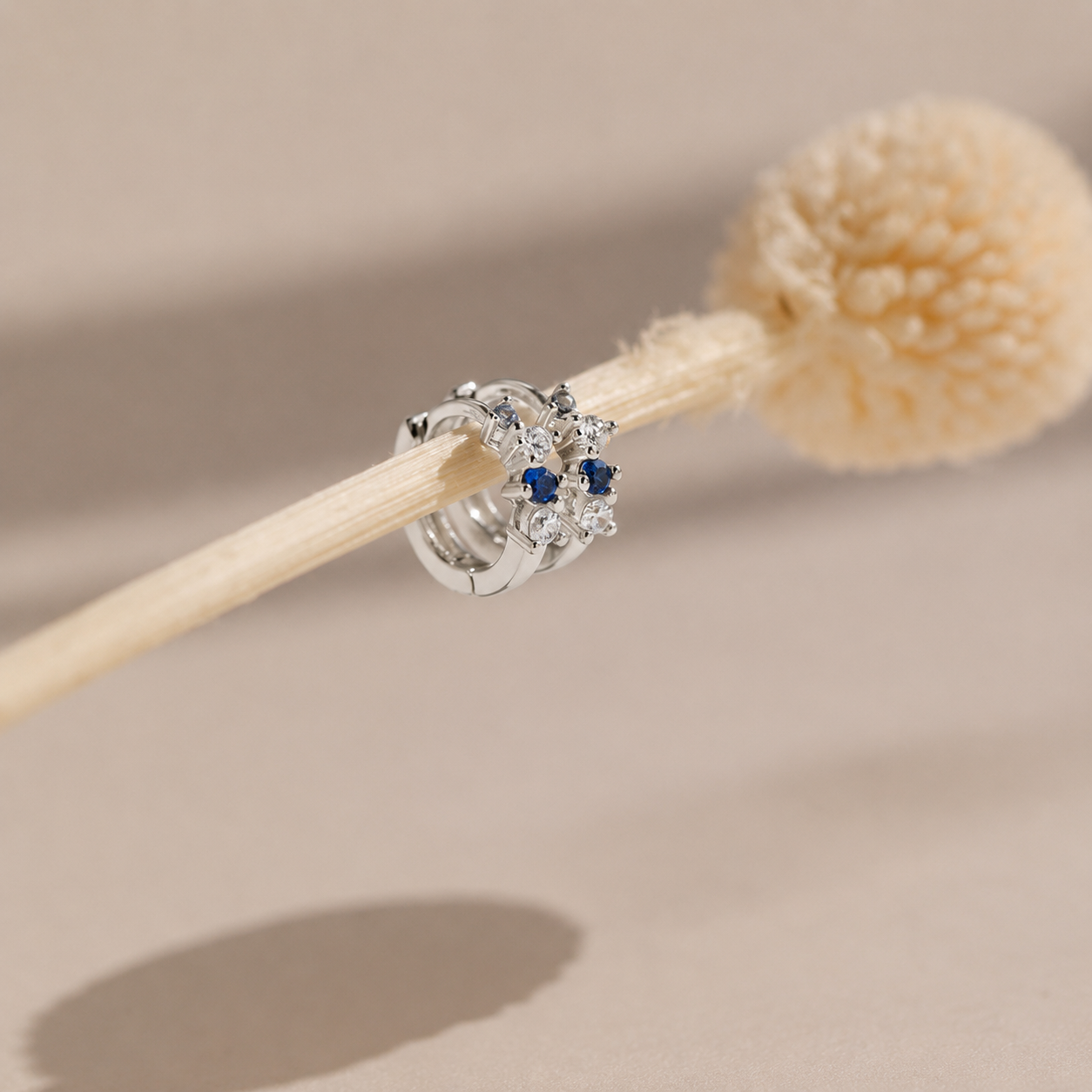 Silver earrings with blue gemstones on a wooden stick against a beige background