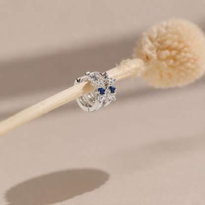 Silver earrings with blue gemstones on a wooden stick against a beige background