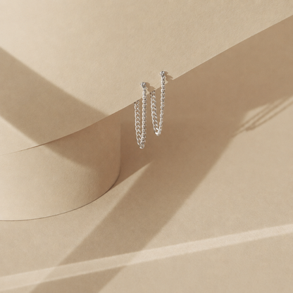 Silver hoop earrings on a beige surface with soft shadows