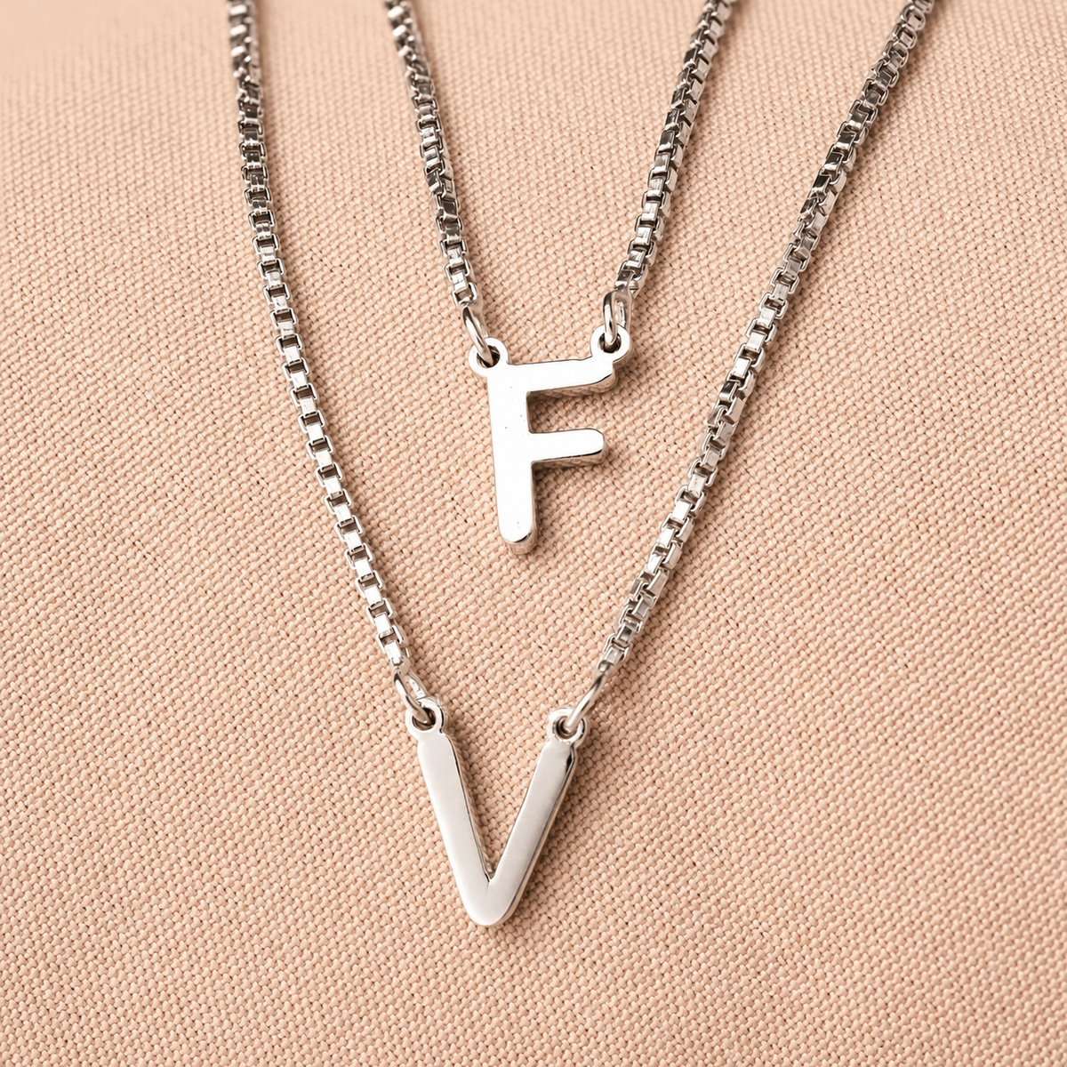 Two silver necklaces with 'F' and 'V' pendants on a beige background