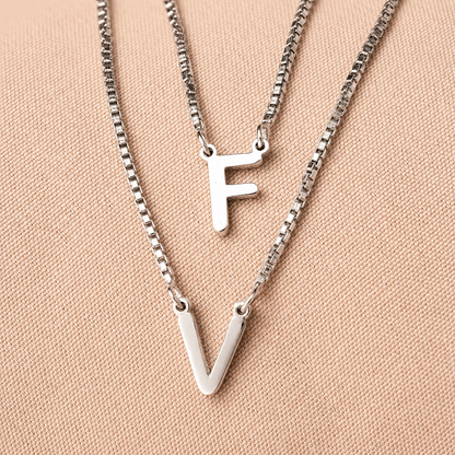 Two silver necklaces with 'F' and 'V' pendants on a beige background