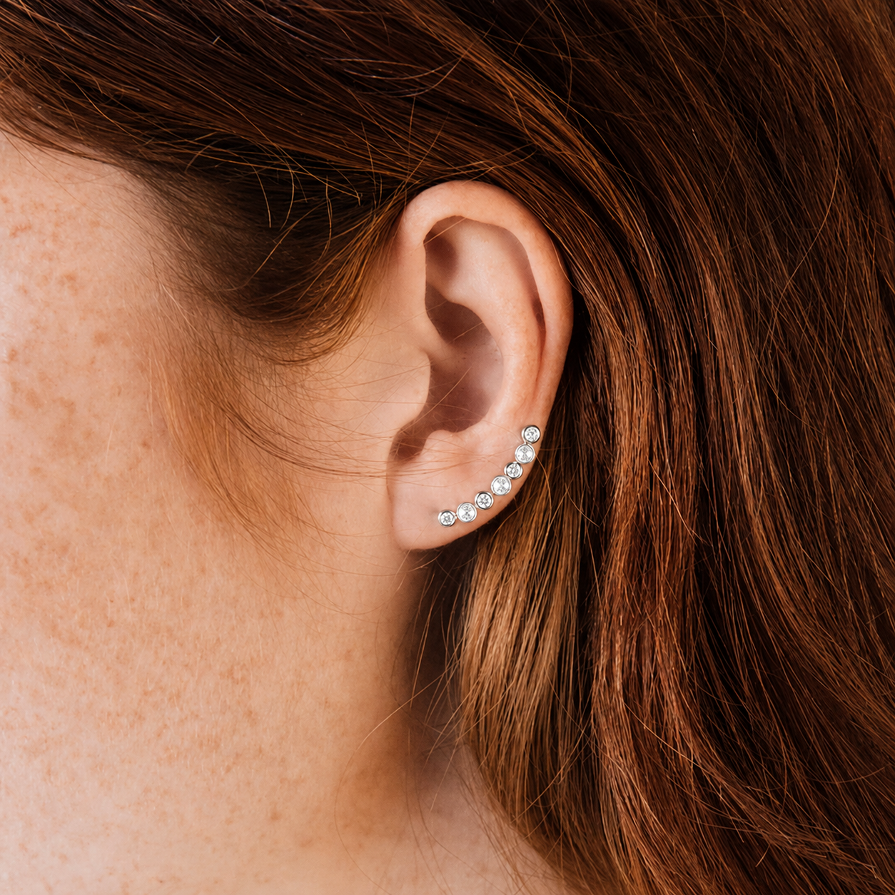 Close-up of an ear wearing a diamond earring with hair partially covering the frame