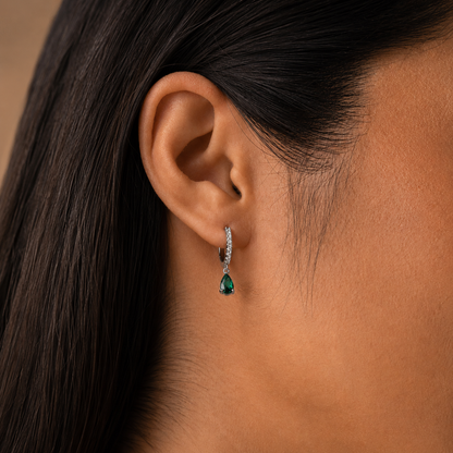 Close-up of an ear wearing a green gemstone earring with a blurred background