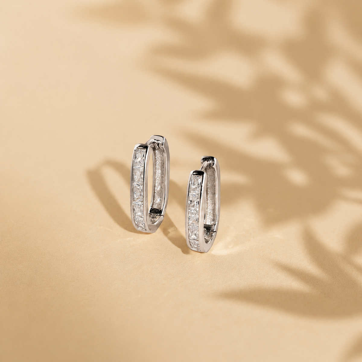Pair of silver hoop earrings with embedded stones on a beige background