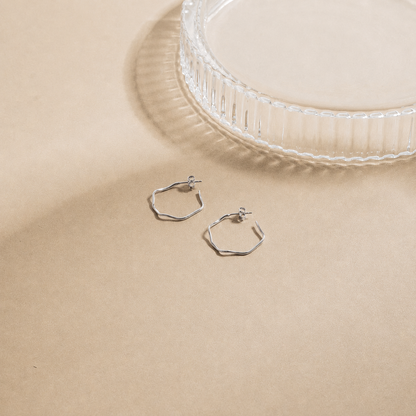 Silver hoop earrings on a beige surface with a clear glass dish in the background