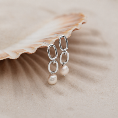 Silver earrings with pearls on a shell background