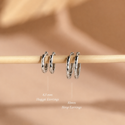 Two pairs of hoop earrings on a wooden stick against a beige background