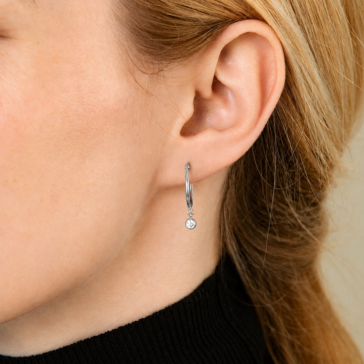 Close-up of a person wearing a silver hoop earring with a small round gemstone.