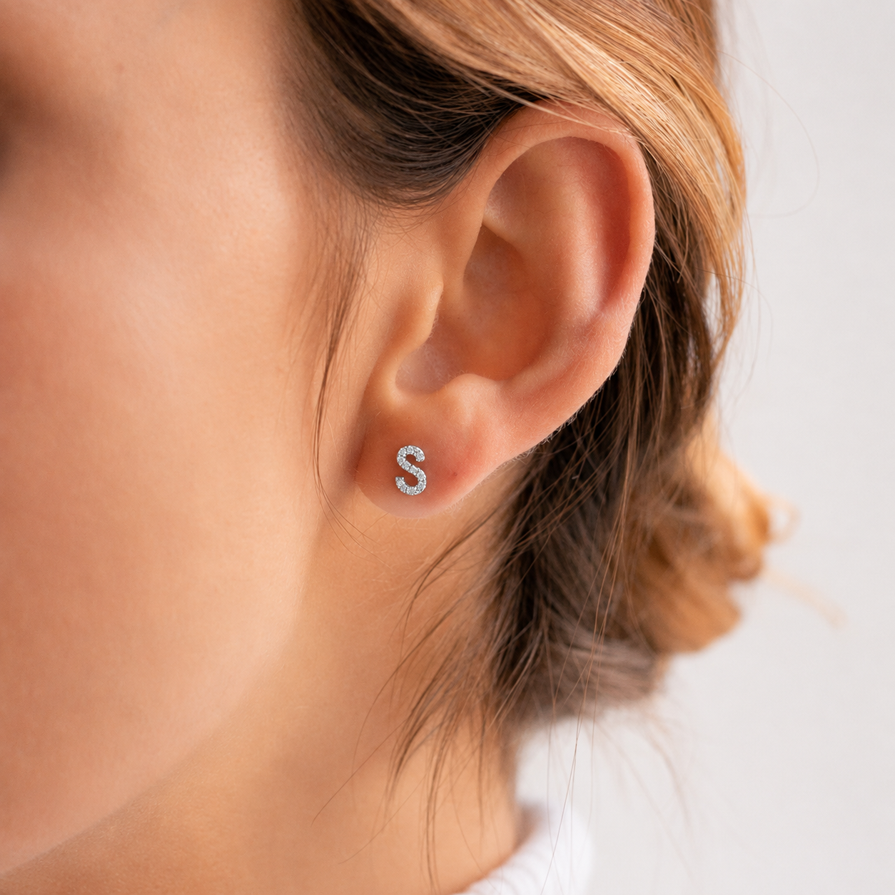 Close-up of an ear wearing a small 'S' earring with a blurred background