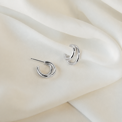 Silver crescent moon earrings on a soft beige fabric background