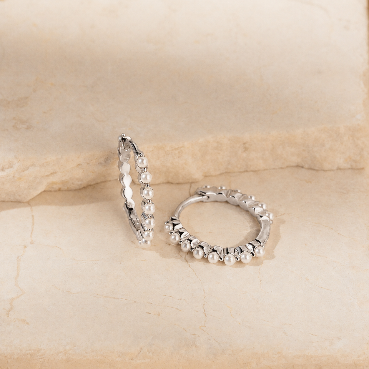 Pair of silver hoop earrings with pearl-like beads on a beige stone background