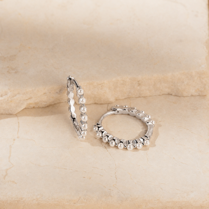 Pair of silver hoop earrings with pearl-like beads on a beige stone background