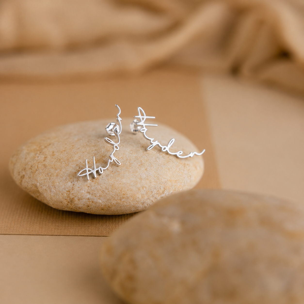 Silver earrings with engraved names on a stone surface