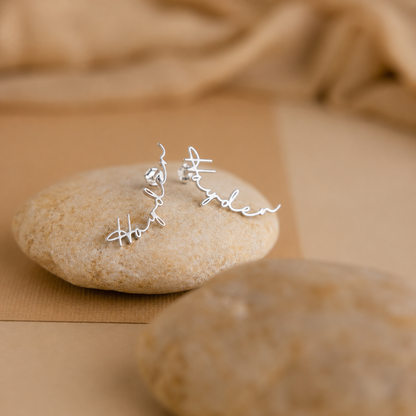 Silver earrings with engraved names on a stone surface