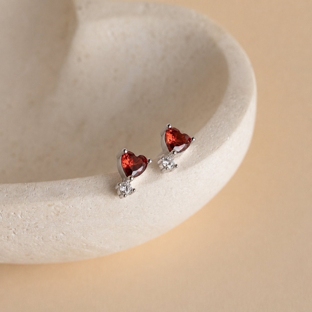 Heart-shaped red gemstone earrings on a beige stone surface