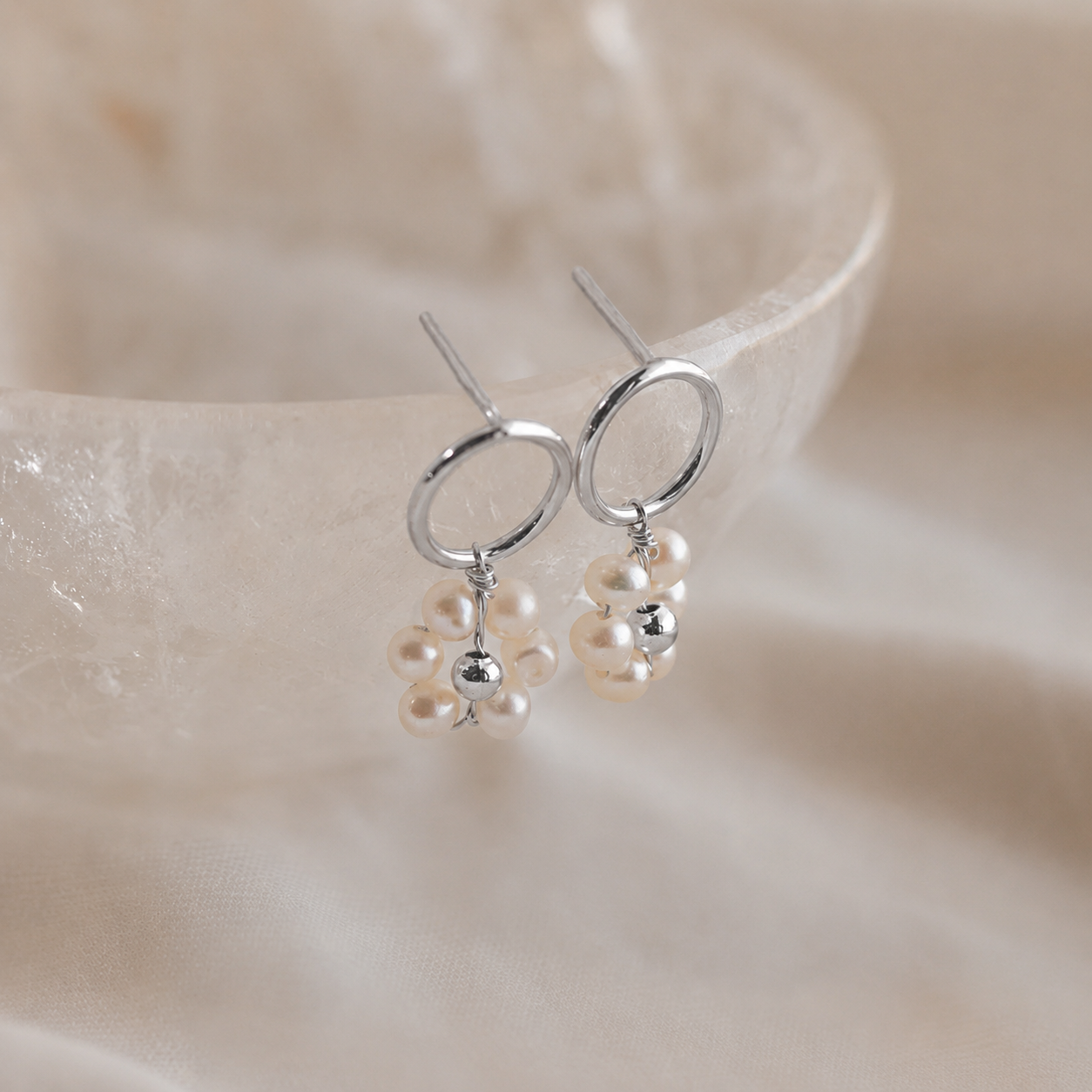 Silver earrings with pearl drops on a soft beige background