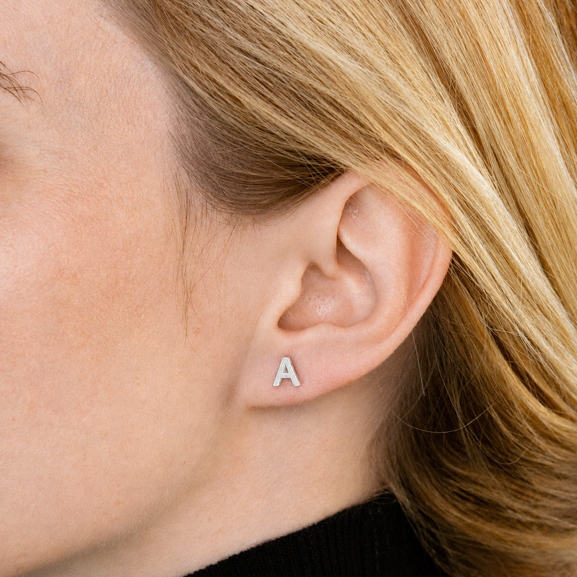 Close-up of an ear wearing a silver 'A' earring with blonde hair.