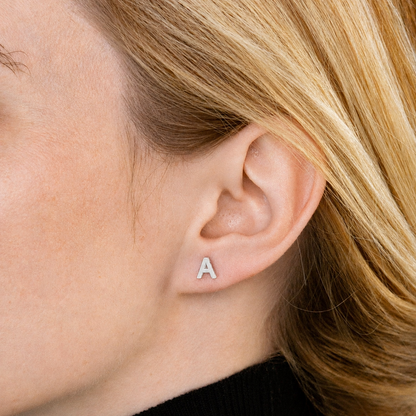 Close-up of an ear wearing a silver 'A' earring with blonde hair.