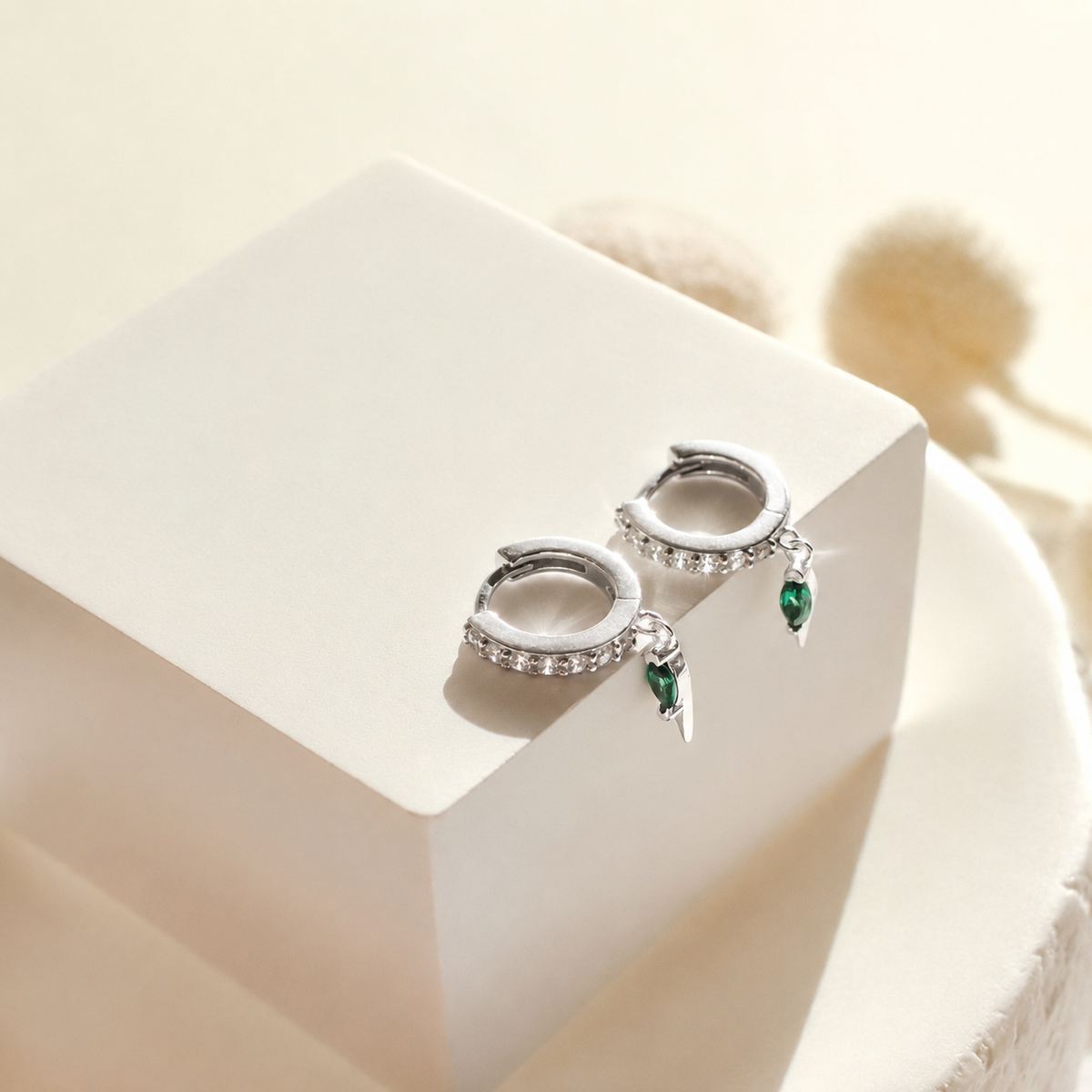 Silver hoop earrings with green gemstones on a white surface